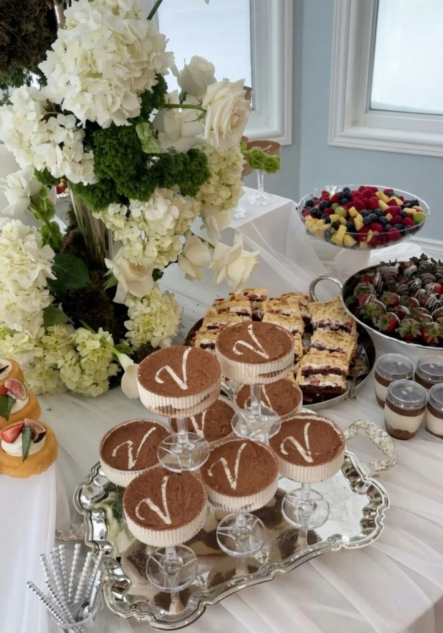 Monogrammed coupe desserts on a silver tray beside flowers and cakes