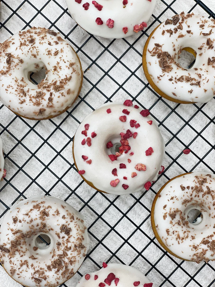 White-glazed small ring cakes decorated with red fruit pieces and chocolate shavings
